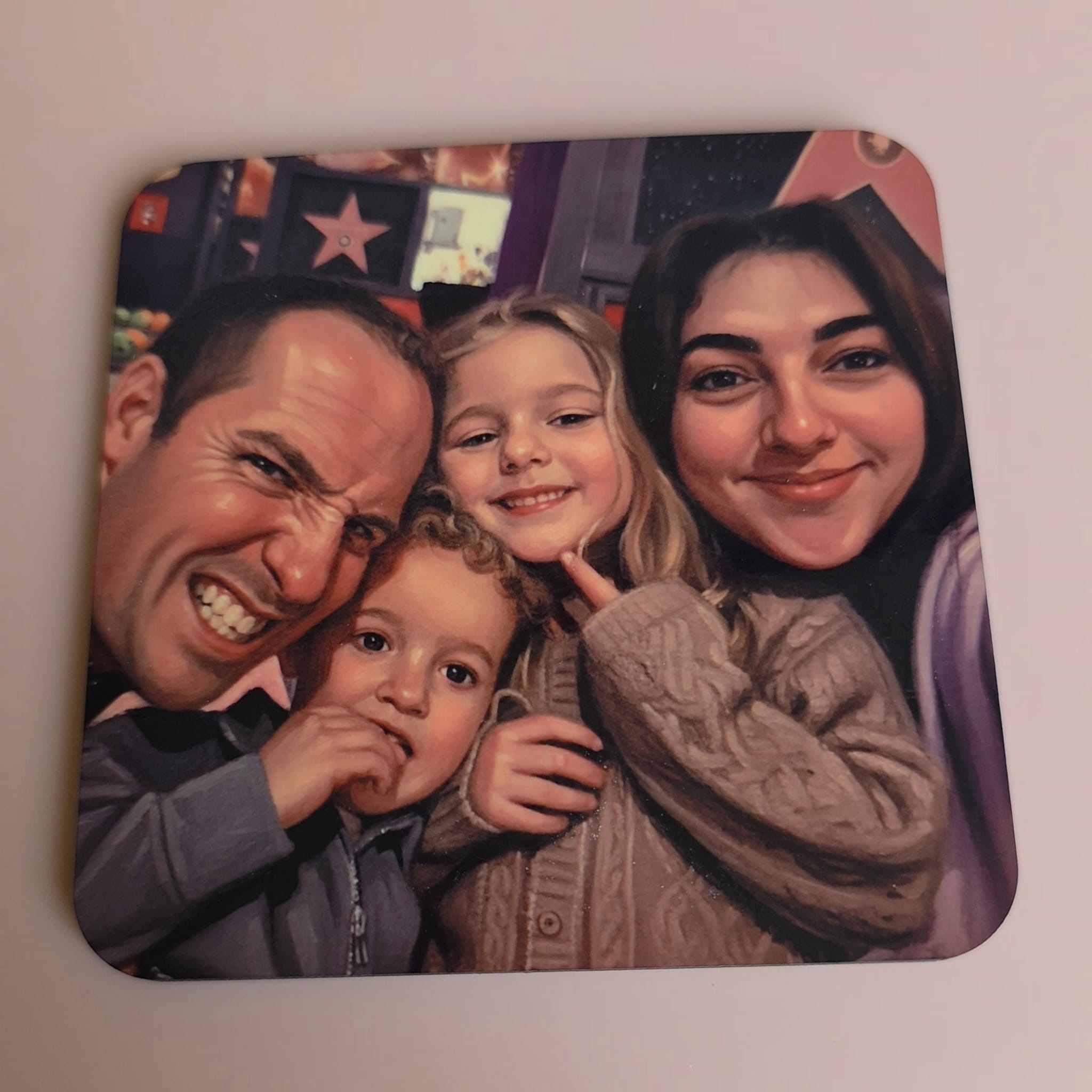 A square coaster with rounded corners featuring a printed custom family portrait, shown on a plain off-white surface.