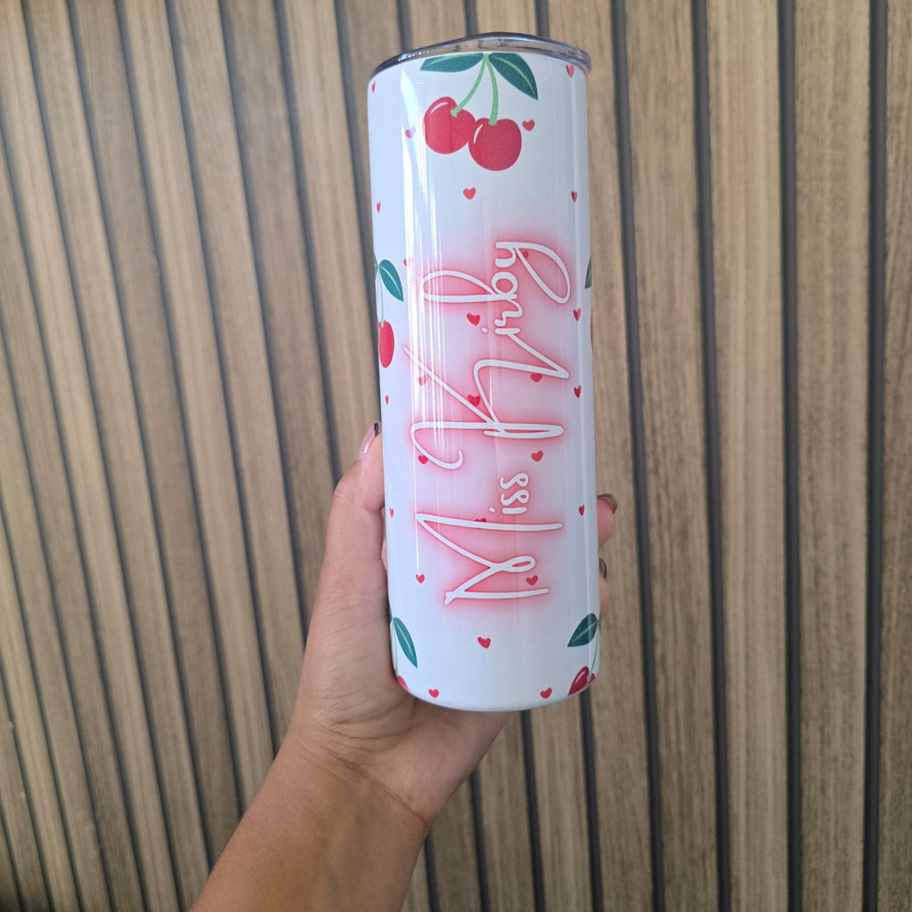 A hand holding a tall white insulated tumbler with cherry illustrations and the text 'Miss Ruby' in pink script, set against a wooden slat background.