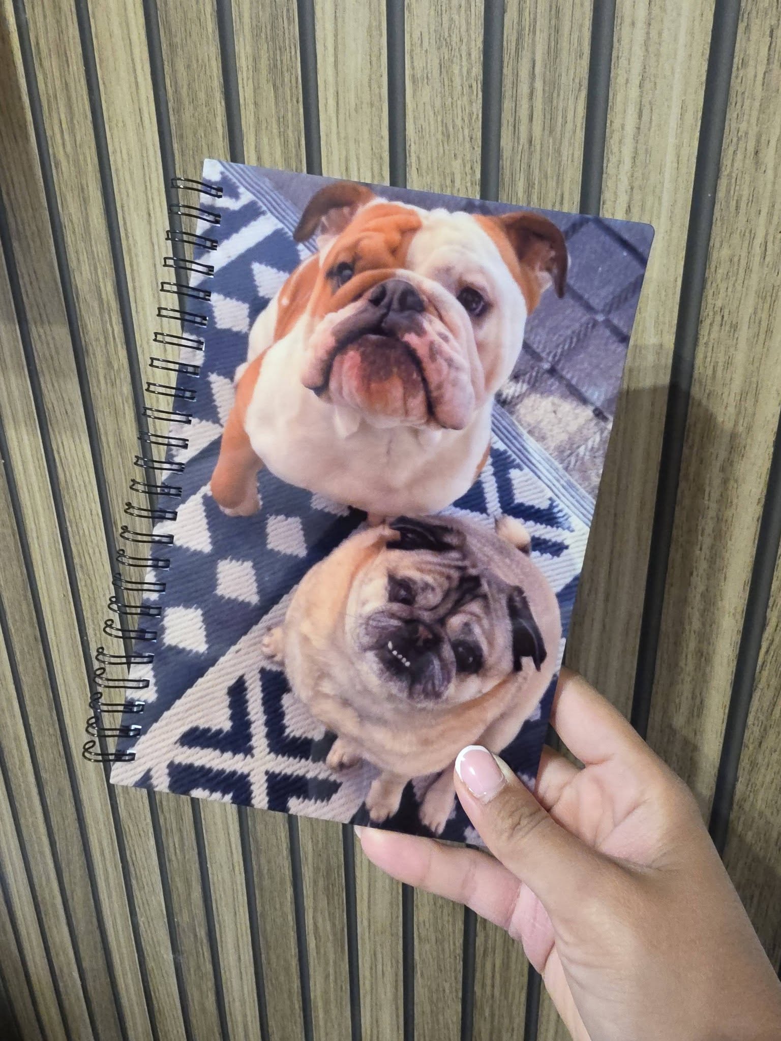 Notebook with a dog design held by a hand against a striped background